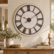 Rustic Wooden Clock With Aged Numerals And Hands above a wooden sideboard with olive branches in a stone jug, a wooden bowl, books and a pillar candle
