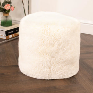 White textured ottoman on a wooden floor with books and a vase in the background.