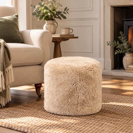 Beige sheepskin pouffe in a cosy neutral living room, styled beside a cream armchair on a natural woven rug