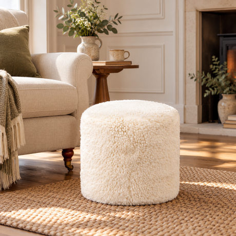 Ivory sheepskin pouffe in a cosy neutral living room, styled beside a cream armchair on a natural woven rug.