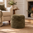 Khaki green sheepskin pouffe in a cosy neutral living room, styled beside a cream armchair on a natural woven rug.