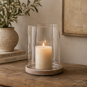 Candle in a glass lantern on a wooden surface with a plant and books in the background.