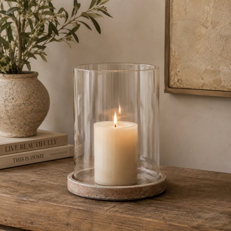 Candle in a glass lantern on a wooden surface with a plant and books in the background.