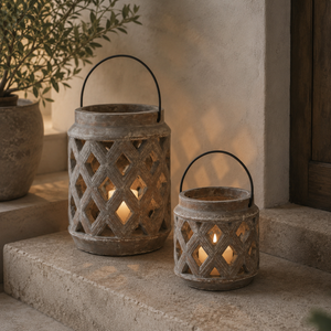 Two rustic lanterns on a stone surface with a plant in the background