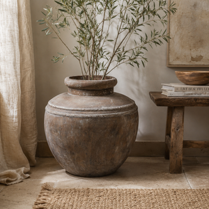 Decorative vase with plants on a rug in a room with a wooden bench and books.