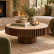 Solmere round travertine and mango wood coffee table styled with books, a candle and a vase in a living room