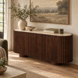 Solmere curved sideboard with travertine top and ribbed mango wood, styled with a vase, bowl and books beneath a landscape painting