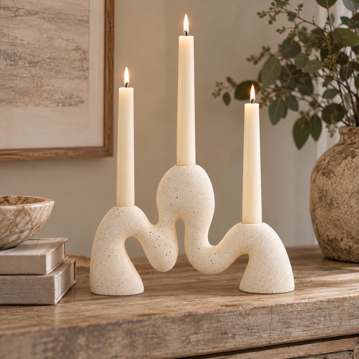 Soren Cream Organic Candle Holder with three lit cream pillar candles in its sculptural wavy, speckled form, set on a rustic wooden table in a warm, styled interior.