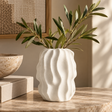 Soren White Textured Bud Vase with a wavy, organic texture, holding green olive branches on a marble tabletop in a warm, sunlit room.