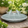 Decorative stone bird bath with two birds on a wooden surface surrounded by flowers