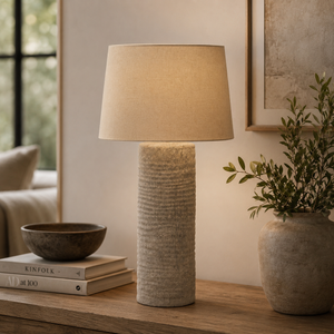 Textured table lamp on a wooden surface with books and a plant in a home setting