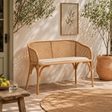 Wicker bench with cushion on a patio with plants and a wall art piece.