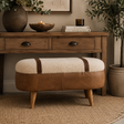 A brown leather and cream bouclé ottoman stool with tapered wooden legs, styled in a warm, rustic living room setting in front of a wooden console table.