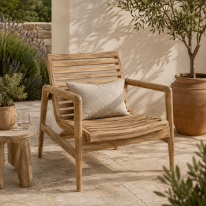 Teak outdoor lounge chair with a slatted back and seat, styled with a neutral cushion on a sunlit patio surrounded by plants and terracotta pots.