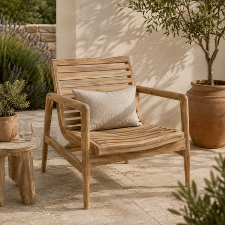 Teak outdoor lounge chair with a slatted back and seat, styled with a neutral cushion on a sunlit patio surrounded by plants and terracotta pots.