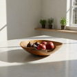 Wooden bowl with fruits on a light surface with plants in the background
