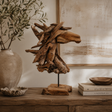 Rustic wooden horse head ornament displayed on a wooden console table in a warm neutral interior, with textured artwork, books and natural decor.