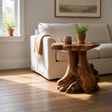 A rustic teak root side table with a mug and a plant in front of a cream sofa with a rug, and light coming through a window.