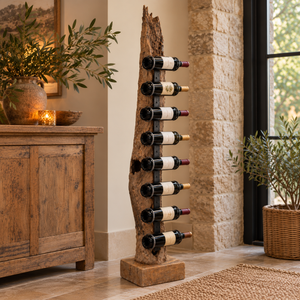 Teak Tree Root Wine Rack holding eight bottles of wine, standing beside a rustic wooden sideboard in a warm neutral room with a stone wall and a potted olive tree