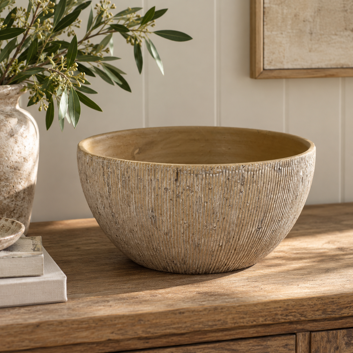 Textured beige decorative bowl styled on a rustic wooden console table in a warm neutral interior.