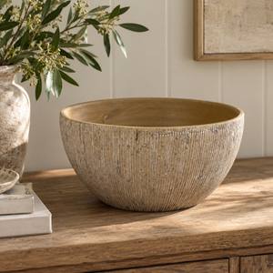 Textured beige decorative bowl styled on a rustic wooden console table in a warm neutral interior.