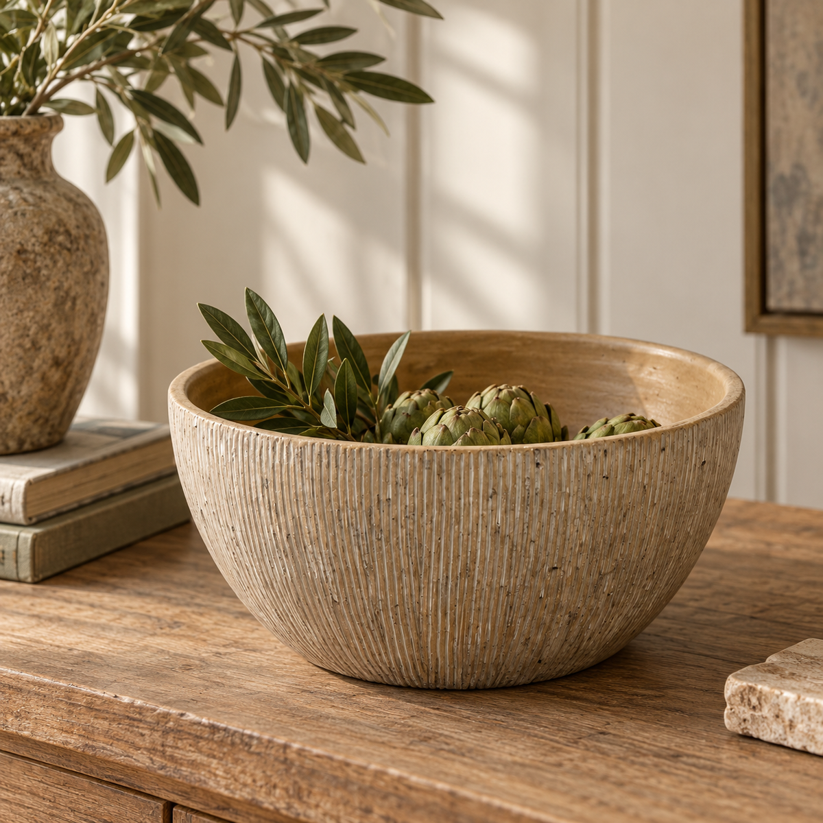Ribbed beige decorative bowl styled on a rustic wooden table with olive branches and artichokes, showcasing its textured finish and warm neutral tones.