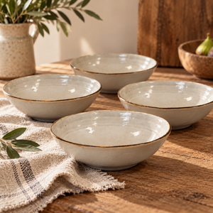 The Gable Collection Set of Four Stoneware Cereal Bowls, four soft beige bowls with brown rims arranged on a rustic wooden table with a linen cloth.