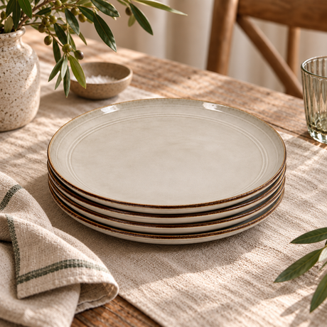 The Gable Collection Set of Four Stoneware Dinner Plates, stacked on a linen runner on a rustic wooden table with olive branches in a speckled vase.