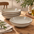 The Gable Collection Set of Four Stoneware Pasta Bowls, three stacked and one in front showing the ridged rings and brown rim, on a rustic wooden table.