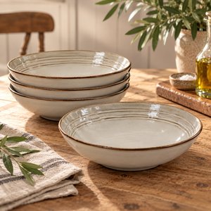 The Gable Collection Set of Four Stoneware Pasta Bowls, three stacked and one in front showing the ridged rings and brown rim, on a rustic wooden table.