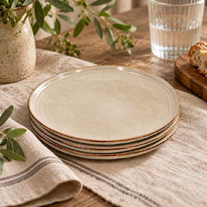 The Gable Collection Set of Four Stoneware Side Plates, stacked on a striped linen runner beside a glass of water, bread and olive branches.