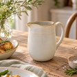 The Gable Collection Stoneware Jug, a soft beige jug with ridged bands, a brown rim and a curved handle, on a rustic wooden table.