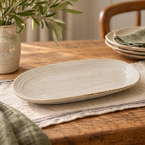 The Gable Collection Stoneware Medium Oval Platter, an empty soft beige oval platter with ridged rings, on a linen runner.