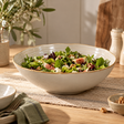 The Gable Collection Stoneware Salad Bowl, filled with a leafy green salad on a rustic wooden dining table with olive branches.