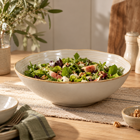 The Gable Collection Stoneware Salad Bowl, filled with a leafy green salad on a rustic wooden dining table with olive branches.