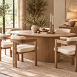 The Hawthorn Grey Mango Wood Oval Dining Table with its reeded pedestal base, surrounded by bouclé dining chairs on a jute rug, with a stone vase of olive branches and candlesticks in a sunlit dining room.