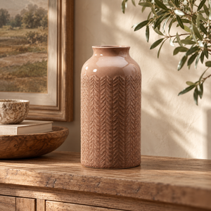 Dusky pink ceramic vase with carved leaf pattern displayed on a rustic wooden console in a warm, neutral country-style interior.