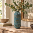 Teal speckled ceramic vase with raised blue-grey and earthy brown detailing, styled with eucalyptus and delicate white flowers on a rustic wooden console table