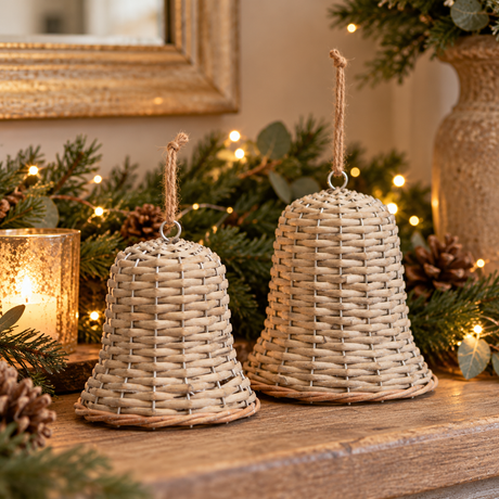 Small and large woven wicker bells on a mantel with a pine garland, fairy lights and a candle