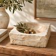 Tivoli Travertine Rough Edge Square Bowl, styled on a wooden table with olive branches and dried olives inside, next to a matching textured ceramic vase and books.