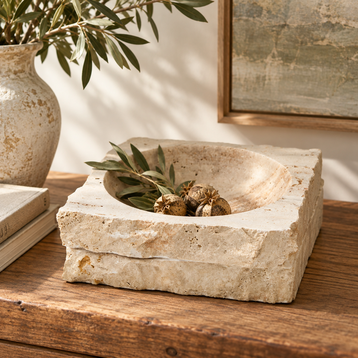 Tivoli Travertine Rough Edge Square Bowl, styled on a wooden table with olive branches and dried olives inside, next to a matching textured ceramic vase and books.