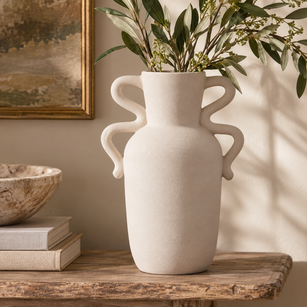 Tova White Tall Vase with Abstract Handles styled on a rustic wooden console with leafy branches.