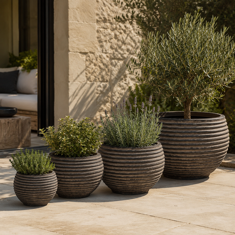 A set of four dark brown ribbed outdoor planters with plants in on a Mediterranean style patio