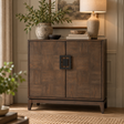 An antique grey wooden sideboard cabinet with a geometric black metal handle, styled in a warm, elegant room with a lamp, potted plant, and books on top.