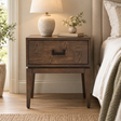 Verona Antique Grey Bedside Table beside a bed, styled with a ceramic table lamp, a small vase of greenery and a book