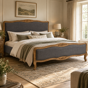 The Vienne Grey Fabric Super King Size Bed with a carved oak frame and grey upholstered headboard and footboard, dressed in cream and sage bedding in a country bedroom.