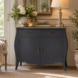 A dark grey wooden cabinet with curved legs, two drawers, and two doors, styled in a bright living room setting with a lamp, flowers, and a mirror.