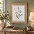 Watercolour Delicate Fern In Washed Wood Frame above a rustic wooden sideboard with olive branches in a stone vase, a linen table lamp and trailing ivy