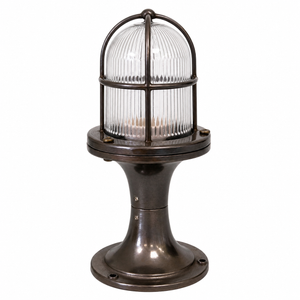 An industrial nautical-style table lamp with a ribbed clear glass dome under a dark bronze metal cage, mounted on a matching dark bronze flanged base.