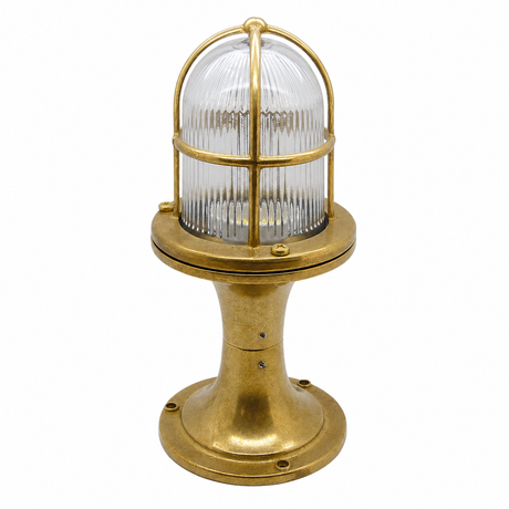 A vintage-style industrial maritime light fixture with a polished brass base and cage, featuring a ribbed clear glass dome shade, isolated on a white background.
